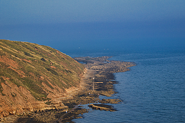 Coastal landscape with a serene blue ocean beside a rugged cliff under a clear sky in Filey, England.