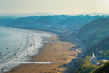 Scenic view of a crowded beach with hills in the background on a sunny day in Filey, England.