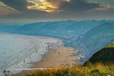 Scenic view of a sunlit beach with mountains in the background and dramatic clouds in the sky in Filey, England.