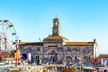 Historic building with clock tower near a ferris wheel under clear blue sky in Hastings, East Sussex, England, United Kingdom, Europe