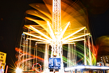 Long exposure of a brightly lit carousel at night, capturing motion blur of spinning lights at a fair.