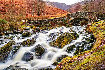 Rustic stone bridge over a flowing stream with mossy rocks in a lush, green landscape in the Lake District, Cumbria, England, United Kingdom, Europe