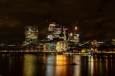 Night time cityscape with illuminated skyscrapers and reflections on water, City of London, England, United Kingdom, Europe