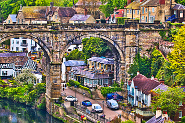 A picturesque view of a quaint village with an old stone bridge arching over a river, surrounded by lush greenery and traditional houses.