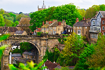 Scenic view of a historic town with an old stone bridge, lush green trees, and traditional buildings.