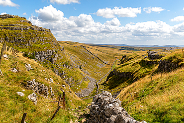 Scenic view of a lush green valley with rocky outcrops under a blue sky with clouds, showcasing natural beauty and tranquility at Malham Cove, Yorkshire, England, United Kingdom, Europe