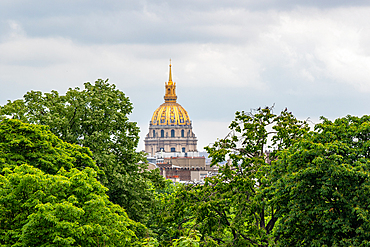 Dome of Les Invalides through lush green trees under a cloudy sky in Paris, France, Europe