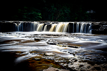 Silky smooth waterfall cascading over rocks with a dark, moody forest backdrop, North Yorkshire, England, United Kingdom, Eurpe