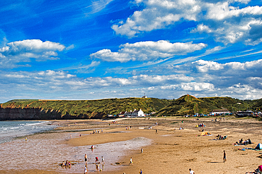 Sunny beach day with blue sky, fluffy clouds, and people enjoying the seaside in Saltburn-by-the-Sea, England.