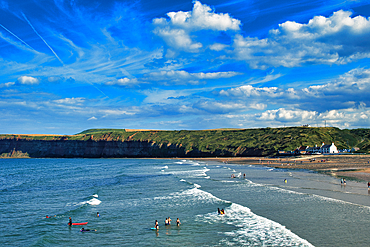 Scenic coastal landscape with blue sky, fluffy clouds, and people enjoying the water at a beach with cliffs in the background in Saltburn-by-the-Sea, England.