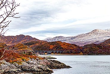 Serene landscape with a tranquil lake, autumnal trees, and distant snow-capped mountains under a cloudy sky in Scotland, United Kingdom, Europe