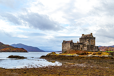 Majestic ancient castle by a serene lake with cloudy skies and mountainous backdrop, Eilean Donan, Dornie, Scotland, United Kingdom, Europe