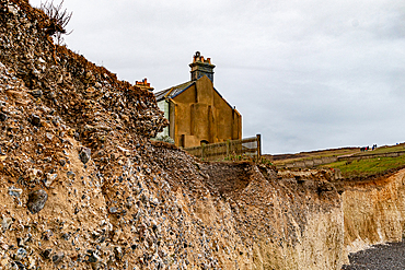 Old coastguard cottage on the edge of a cliff with eroded soil, under a cloudy sky, Birling Gap, Seven Sisters, East Sussex, England, United Kingdom, Europe