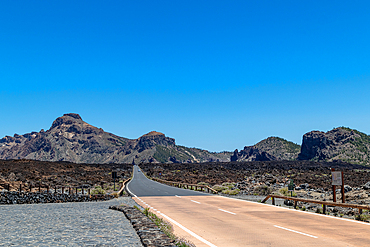 Desert road stretching into the distance with rocky mountains under a clear blue sky in Tenerife, Canary Islands, Spain, Atlantic, Europe