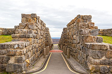 Stone pathway leading through ancient wall ruins under a cloudy sky, with a scenic view in the distance, North Yorkshire, England, United Kingdom, Europe