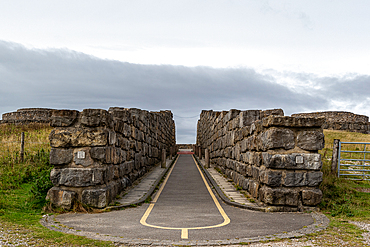 Empty road leading through stone gateways under a cloudy sky, North Yorkshire, England, United Kingdom, Europe