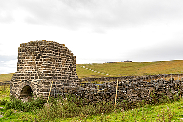 Ancient stone kiln in a rural field with a dry stone wall and overcast sky, North Yorkshire, England, United Kingdom, Europe