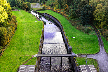 Aerial view of a lush green park with a meandering stream and a small bridge, showcasing serene nature scenery at Thruscross Reservoir in North Yorkshire, England, United Kingdom, Europe