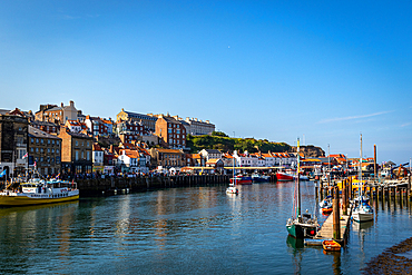 Quaint coastal town with historic buildings along a serene harbour, boats moored on clear water under a blue sky in Whitby, Yorkshire, England, United Kingdom, Europe