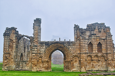 A foggy scene of ancient stone ruins with arched doorways and windows, surrounded by green grass.