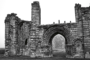 Black and white photo of ancient stone ruins with archways and weathered walls, set against a foggy background.