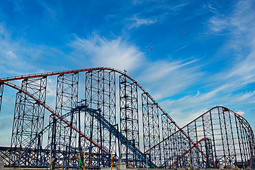 A vibrant roller coaster with red and blue tracks against a bright sky with wispy clouds. The structure is tall and intricate, showcasing the excitement of amusement parks.