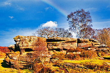 Scenic view of a rocky outcrop with a lone tree against a blue sky with a faint rainbow in the countryside at Brimham Rocks, in North Yorkshire