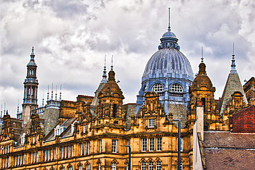 A close-up view of historic architecture featuring ornate domes and spires against a cloudy sky. The building showcases intricate stonework and a mix of architectural styles.