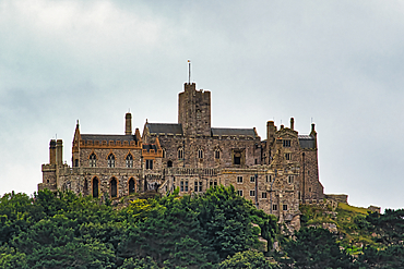 A majestic castle perched on a hill, surrounded by lush greenery under a cloudy sky. The architecture features a mix of stone walls and towers, showcasing historical design elements.