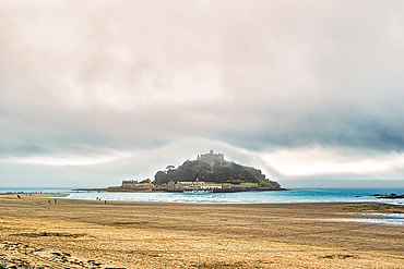 A scenic view of a coastal landscape featuring a small island with a castle, surrounded by water and sandy beach. The sky is overcast with a misty atmosphere, creating a serene and tranquil setting.