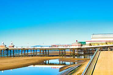 Serene seaside pier with clear blue sky reflected in calm water, showcasing tranquil coastal scenery in Blackpool, England