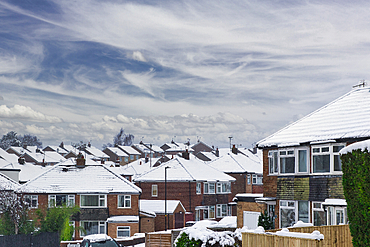 Snow-covered suburban houses under a cloudy sky. Brick houses with snow on their roofs and window sills. A residential street scene in winter in Harrogate, UK.