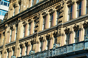 Detailed facade of a building with ornate stonework, multiple windows, and a balcony. The composition emphasizes architectural details and symmetry in Manchester, UK.