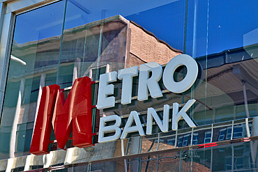 A close-up showcases the 'Metro Bank' sign displayed on a reflective glass window, capturing a building reflection in the glass in Liverpool, UK.