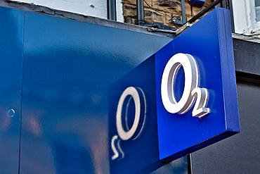 Close-up of a blue sign with the O2 logo; the logo is illuminated and casts a shadow onto the building facade in Harrogate, Yorkshire, UK.