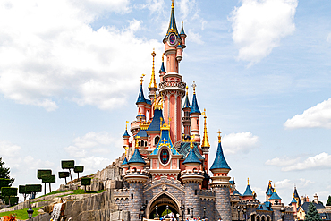 Full shot of Sleeping Beauty Castle at Disneyland Paris, showcasing its pink and blue turrets against a partly cloudy sky.