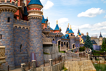 Exterior shot of a castle with stone walls, blue and pink turrets, and a moat on a partially cloudy day at Disneyland Paris.