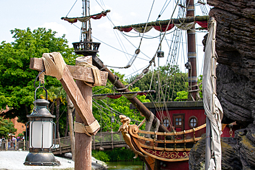 Pirate ship detail featuring lantern, mast and sails, rope accents, and green foliage in the background, under a blue sky at Disneyland Paris.