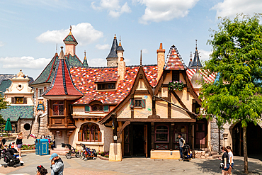 Exterior shot of fanciful, colorful buildings with a tiled roof in a park setting on a bright day. People are walking nearby at Disneyland Paris.