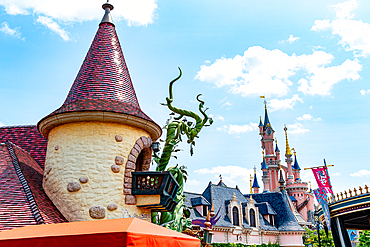 View of castle structures at a theme park. A tan tower and beanstalk sculpture are in the foreground, with a pink castle in the background at Disneyland Paris.