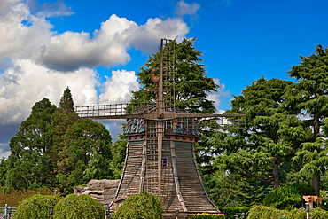 A windmill stands amidst lush greenery under a partly cloudy sky, with its weathered wood and colorful roof adding visual interest at Disneyland Paris, France.