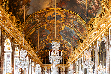 Ornate interior featuring a painted ceiling, chandeliers, and gilded details in a grand hall with arched windows and marble accents at Versailles Palace, Paris.