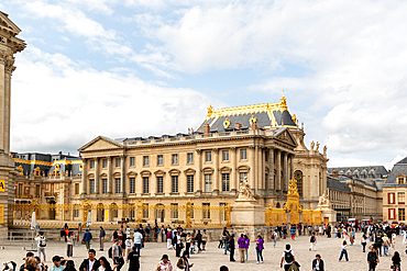 Exterior view of the Palace of Versailles, France, with a crowd of people in the foreground and partly cloudy sky above at Versailles Palace, Paris.