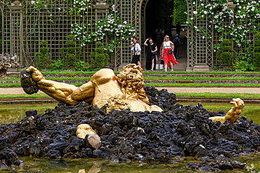 A golden sculpture of a man emerging from black rocks in a pond, with people walking in the background at Versailles Gardens, Paris.