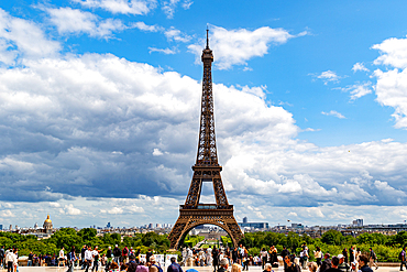 Eiffel Tower view from crowded observation point under a blue, cloudy sky. Cityscape in background.