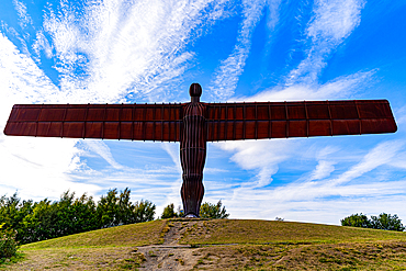 The image features the Angel of the North statue standing on a grassy hill against a blue sky with streaky white clouds.