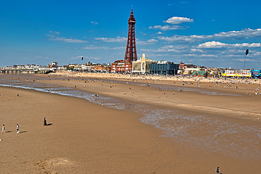 View of Blackpool beach with the Blackpool Tower rising above the cityscape on a sunny day with people enjoying the seaside.