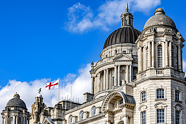 A monumental stone building with domes and flags against a bright blue sky with scattered clouds in Liverpool, UK.