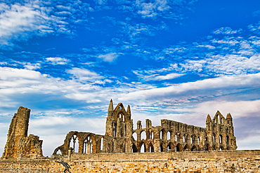 Ruined abbey against a vibrant blue sky with scattered white clouds, featuring stone arches and spires in Whitby, UK.