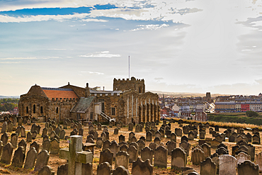 A stone church and a vast graveyard with weathered headstones overlook a colorful coastal town under a wide sky in Whitby, UK.